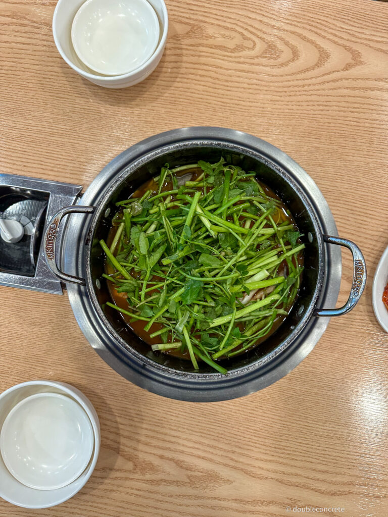 테이블 위에 올려진 버섯매운탕 냄비, 신선한 미나리가 듬뿍 올려져 있다.