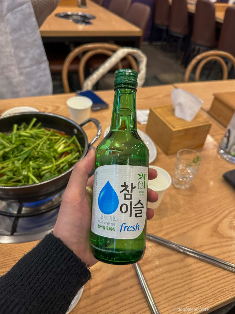 손에 들린 참이슬 소주 병과 테이블 위의 버섯매운탕 냄비.