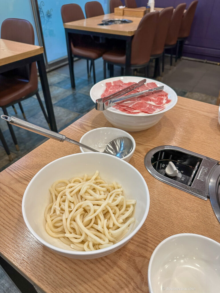 테이블 위에 칼국수 면과 소고기 샤브샤브가 담긴 그릇이 놓여 있다.