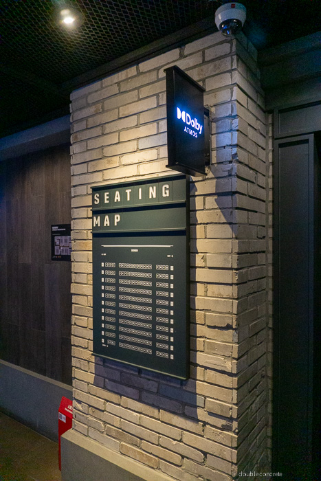 벽돌 인테리어 벽면에 Dolby ATMOS 로고가 빛나고 있으며, 그 아래 **SEATING MAP (좌석표)**가 부착되어 있다. 좌석표에는 상영관의 좌석 배치도가 세부적으로 나열되어 있어, 관람객들이 자신의 좌석 위치를 쉽게 확인할 수 있도록 구성되어 있다.