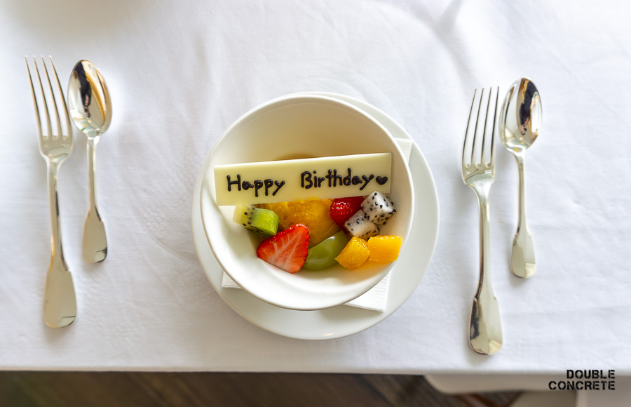 하얀 초콜릿 판에 생일 축하 메시지가 적혀있고, 다양한 신선한 과일이 담긴 디저트.