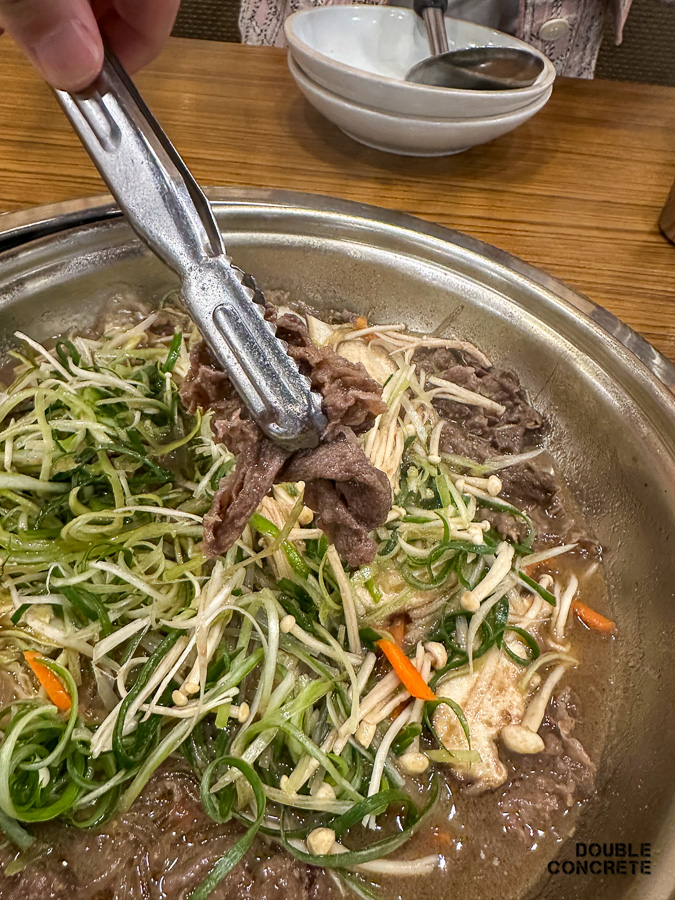 한우불고기 전골에서 고기를 집게로 들어올린 장면