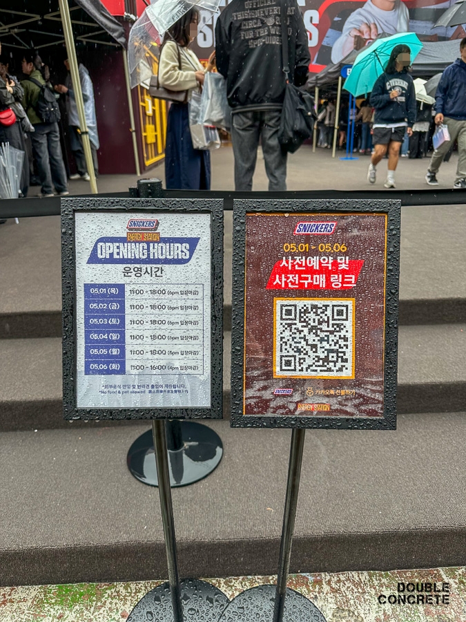 스니커즈 팝업 운영 시간표와 QR코드 사전예약 안내판이 비에 젖은 상태로 세워져 있는 모습